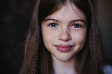 Portrait of a beautiful young girl with dark hair and blue eyes on a dark background, close up