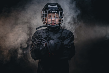 Young blonde sporty boy, ice hockey player, posing in a dark studio for a photoshoot, wearing an...