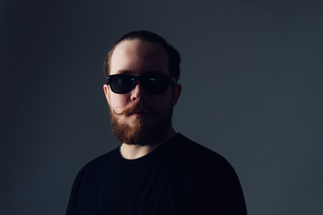 Handsome young man with a beard and mustache in sunglasses in fashionable clothes.
