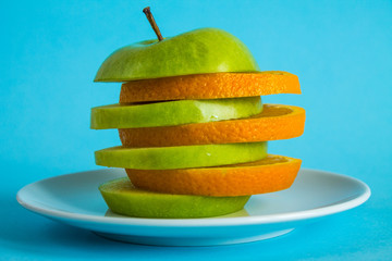 Fototapeta na wymiar Alternating slices of apples and oranges on a white plate in close-up on a bright blue background. Concept - healthy food, vitamins, fruits, mix
