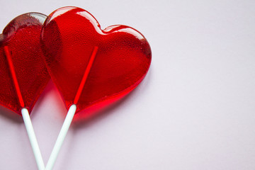 Two transparent lollipops on red sticks in the shape of hearts on a light background with copy space