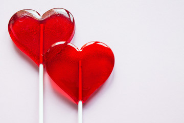 Two transparent lollipops on red sticks in the shape of hearts on a light background with copy space
