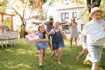 Small children ruunning with present outdoors in garden on birthday party.