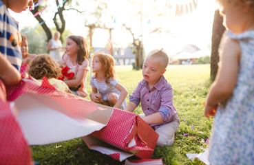Down syndrome child with friends on birthday party outdoors, opening presents.