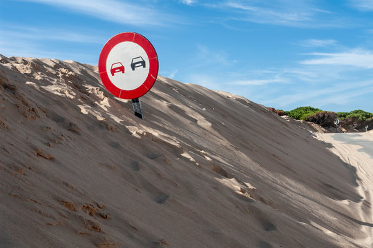 Señal de trafico prohibido adelantar enterrada en la arena de una duna en Tarifa