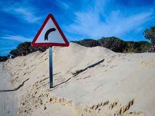 Señal de trafico precaución curva a la derecha enterrada por arena de las dunas de Tarifa