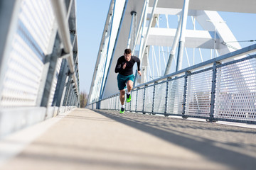 Young male runner sprinting on the bridge in the city during day.
