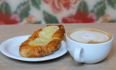 a Cup of coffee a cappuccino and a bun on a plate