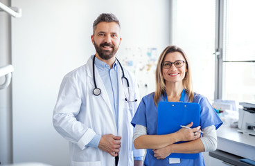 A dentist with dental assistant in modern dental surgery, looking at camera.