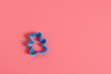 Blue plastic cookie cutter for making cookies in the shape of a teddy bear on a pink background....