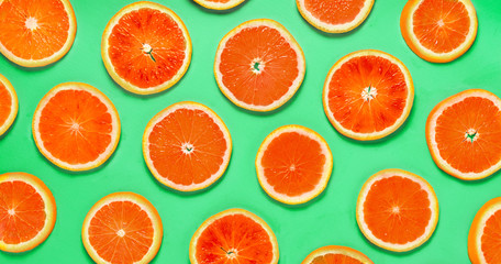 Fruit pattern of red grapefruit citrus slices on green background. Top view.