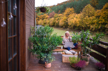 Senior woman with laptop and smartphone sitting outdoors on terrace.