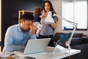 Young family couple having argue about finances at home the husband sits anxious with the laptop and the woman holds the child and complains to him