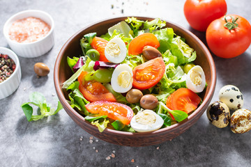Fresh organic green salad with tomatoes, olives and quail eggs on dark stone table with copy space for your text. Healthy food concept.