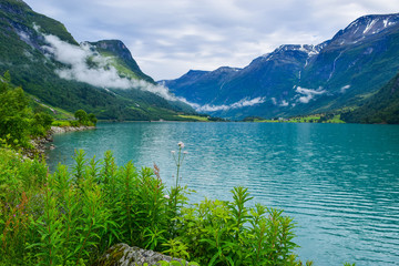 Fototapeta na wymiar Landscape of beautiful Oldevatnet glacial lake and foggy mountains in which there are glaciers of Jostedalsbreen National Park. Norway.