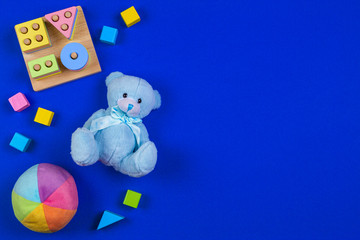 Baby kids toys background. Blue teddy bear, colorful wood blocks, shape color recognition puzzle stacker on navy blue background. Top view