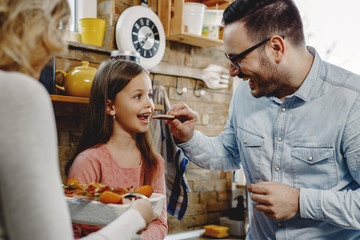 Happy father feeding his daughter in the kitchen.