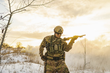Modern war. army Man in camouflage in winter field reloads machine gun. sun backlight and smoke....
