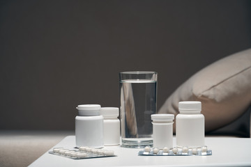 Pills and glass of water near sofa, dark background with copy space