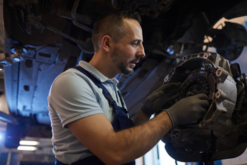 Obraz na płótnie Canvas Low angle portrait of bearded car mechanic repairing gearbox in auto workshop, copy space