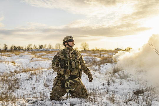 exhausted soldier man after battle fells to knees or kneeling in winter desert. commandos with equipment . Modern warfare battlefield soldier is on his knees and looking to sky