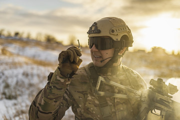 Fototapeta premium Modern war soldier army Man in multicam camouflage speaks on the walkie-talkie radio. equipment commandos with helmet and gun. soldier, sun backlight and smoke. modern warfare. atmosphere of battle