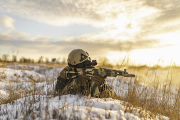 Modern war soldier army Man in multicam camouflage is lying and aiming aim at the sight in winter field. full equipment commandos with helmet and weapon gun. lying and shooting soldier. modern warfare