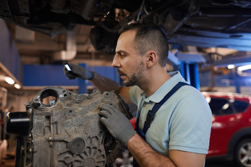 Fototapeta na wymiar Side view portrait of car mechanic inspecting gearbox in auto repair shop, copy space