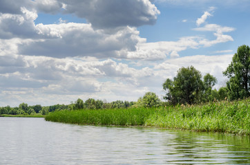 Summer river landscape with uninhabited coast and blue sky with clouds