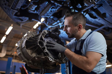 Dramatic low angle portrait of muscular car mechanic inspecting car part in auto repair shop, copy space