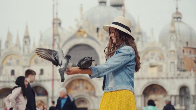 Girl in straw hat feeds pigeons on hand, San Marco. Famous ritual among tourists