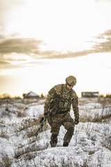 exhausted army soldier Man in multicam camouflage after the battle walks in winter desert. commandos with full equipment helmet and gun watch battlefield. Modern warfare army soldier and battlefield