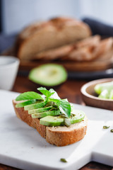 Avocado toast with pepitas and fresh basil on a white marble cutting board. Home cooking, healthy eating concept.