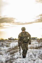 exhausted army soldier Man in multicam camouflage after the battle walks in winter desert. commandos with full equipment helmet and gun watch battlefield. Modern warfare army soldier and battlefield