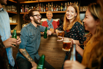 Group of friends drinking beer, chatting and having good time at pub. Night out.