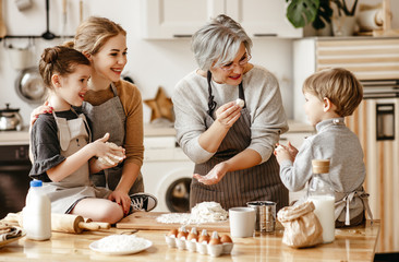happy family a grandmother with her daughter and grandchildren cooks in kitchen, kneads dough,...