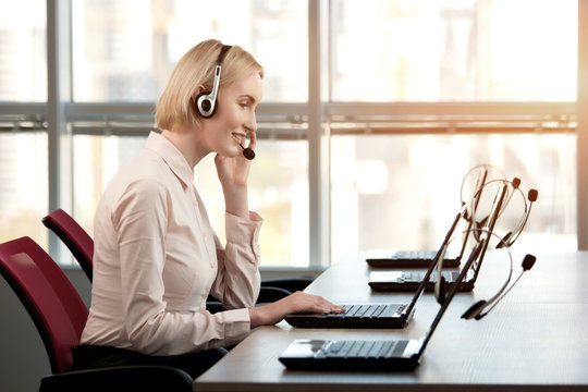 Support Phone Operator In Headset At Workplace. Beautiful Business Woman Working At Her Desk With Headset And Laptop, Profile Side View.