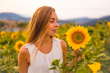 Lifestyle, portrait of a young pretty caucasian blonde with a dress looking at a sunflower