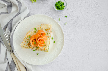 Traditional Russian thin pancakes or crepes with cheese, herbs and smoked salmon on a white plate on a light background. Holiday maslenitsa. Horizontal, top view, copy space