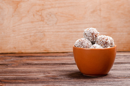 Balls of energy dates, nuts, oats, sprinkled with coconut powder close-up on a wooden background.