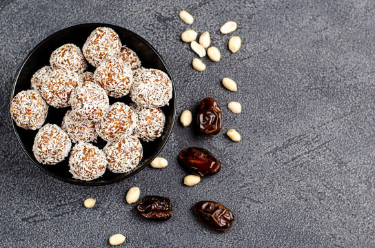 Energy balls in a black plate and ingredients dates, peanut nuts for their preparation on a dark background, flat lay