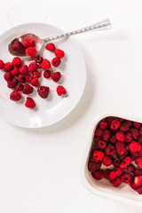 White plate with a silver spoon and a container with raspberries. Fresh summer berries on a white background.