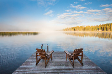 Wooden chairs on dock looking over lake at dawn