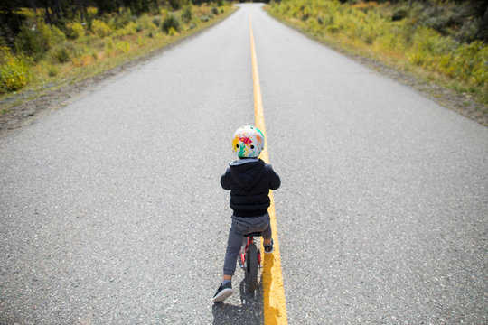 Rear view of young boy biking on paved roadway.