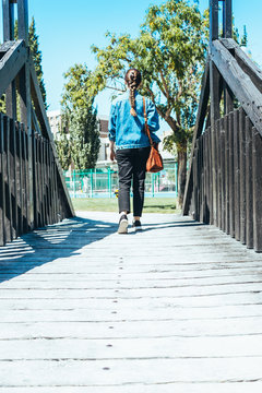 Young woman walking with her brown bag over a wooden bridge in a park