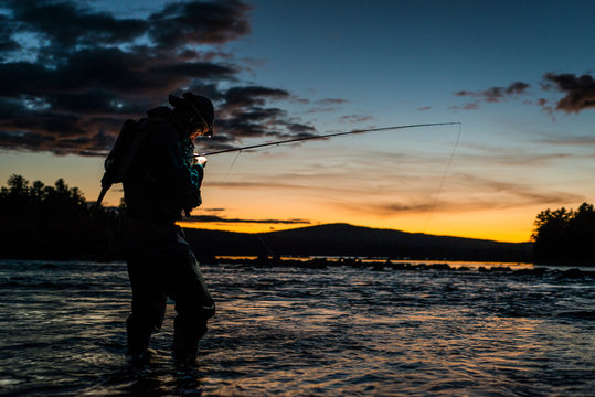 A lone fly fisherman tying on a fly at sunset in Maine.