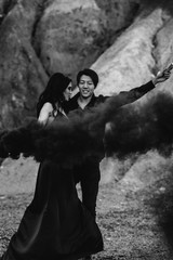 An Asian couple in love lit black smoke bombs in the mountains. Colored smoke. Black-white