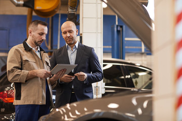 Waist up portrait of car mechanic talking to businessman while using digital tablet in auto repair...