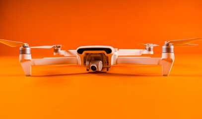 Close-up of white drone on orange background. Modern drone unmanned aerial vehicle with propellers.