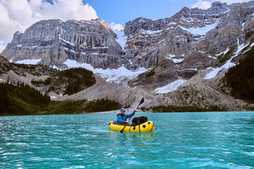 Adventure photographer paddles pack raft across Cirque Lake in Banff.
